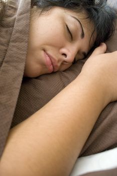 A young brunette woman is fast asleep in her bed.