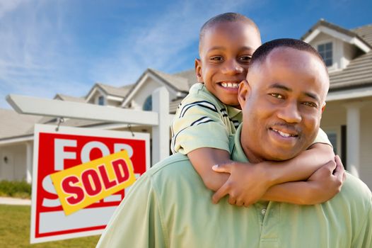 Happy African American Father and Son in Front of New Home and Sold Real Estate Sign.