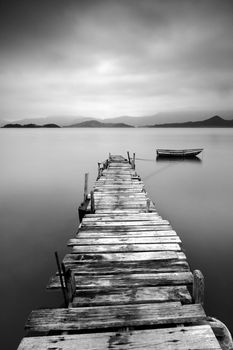 Looking over a desolate peer and a boat, black and white