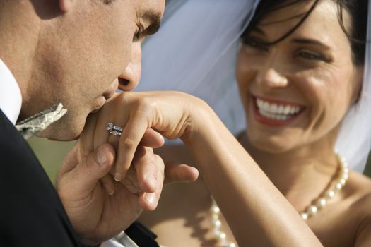 Caucasian prime adult male groom kissing hand of female bride.