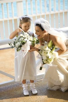 Caucasian mid-adult bride kneeling next to flower girl admiring her flowers.