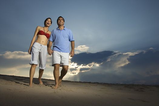 Caucasian mid-adult couple holding hands walking on beach.