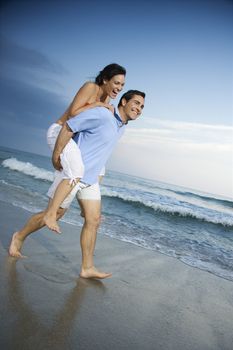 Caucasian mid-adult male carrying female piggyback style on beach.
