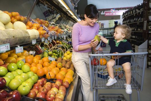 Caucasian mid-adult woman grocery shopping for fruit with young male toddler.