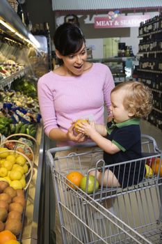 Caucasian mid-adult woman grocery shopping for fruit with young male toddler.