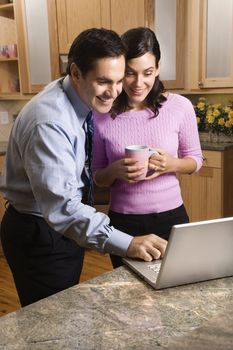 MId-adult couple looking at laptop computer while drinking coffee in kitchen.