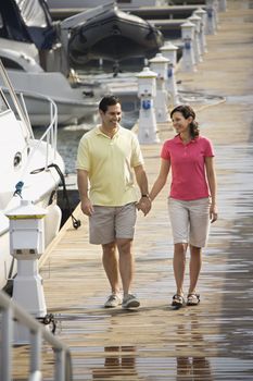 MId-adult Caucasian couple holding hands and walking at harbor.