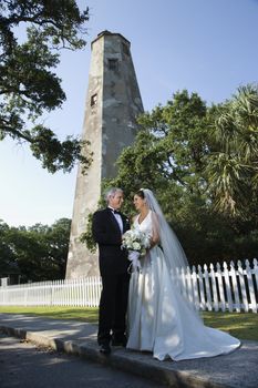 Bride and groom looking at each other with lighthouse in background.