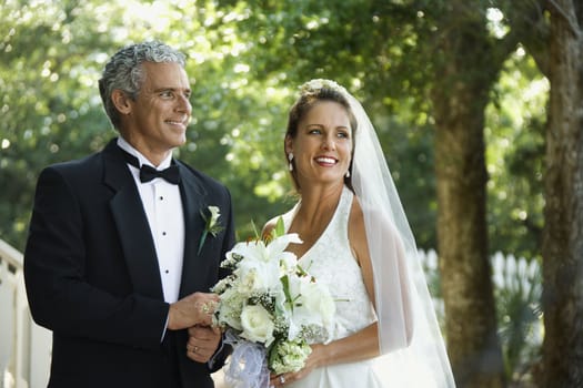 Portrait of bride and groom holding hands outside.