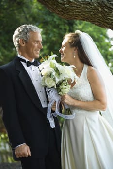 Portrait of a bride and groom smiling at each other outside.