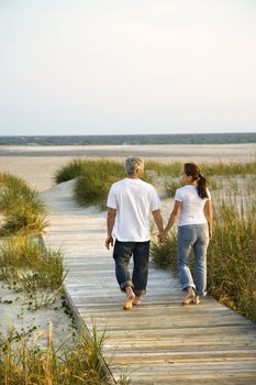 Back view of mid-adult Caucasian couple walking down walkway to beach.