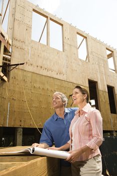 Caucasian mid-adult male and female with blueprints observing building construction site.