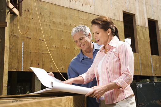 Caucasian mid-adult male and female looking at blueprints in construction phase of house.