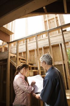 Caucasian mid-adult male and female with blueprints in building construction site.