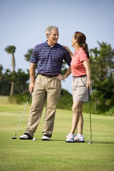 Caucasion mid-adult man and woman standing on golf course talking to each other.