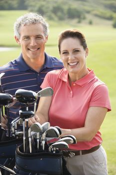 Caucasion mid-adult man and woman with golf clubs smiling and looking at viewer.