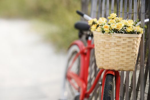 Red vintage bicycle with basket and flowers leaning against wooden fence at beach.