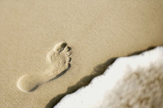 Footprint in sand next to wave.