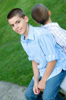 Two brothers sitting back to back on a bench in the park.  