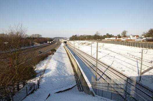 A view of a rail track covered in a layer of snow with a motorway next to it
