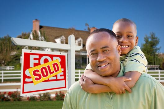 Happy African American Father and Son in Front of New Home and Sold Real Estate Sign.