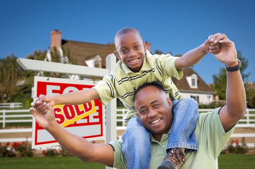 Happy African American Father and Son in Front of New Home and Sold Real Estate Sign.