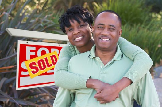 Happy African American Couple in Front of Sold Home For Sale Real Estate Sign.