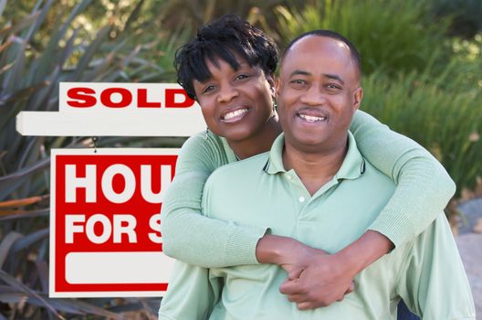 Happy African American Couple in Front of Sold Home For Sale Real Estate Sign.