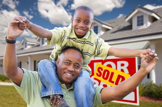 Happy African American Father and Son in Front of New Home and Sold Real Estate Sign.