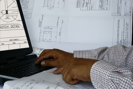 An engineer doing his design on computer with plans and blueprint

