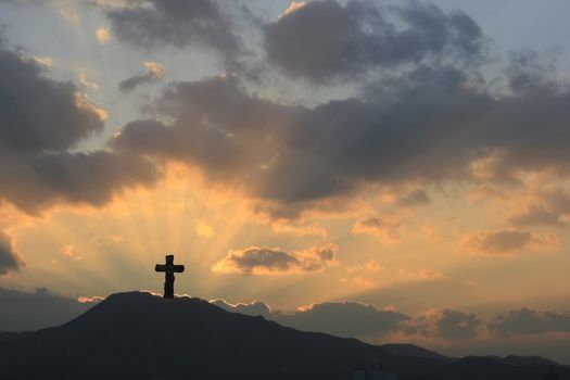 Cross on Dramatic Sunset in a beautiful landscape-mountain and sunbeams rays accentuating through thick clouds.