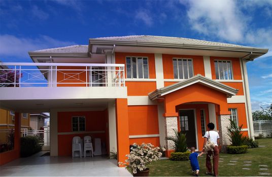 Modern orange house with nice blue sky and family entering the house
