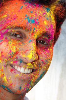 A portrait of a smiling Indian teenager with his face covered with various colors during holi festival.