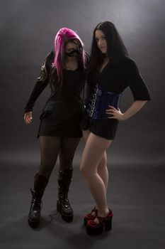 crazy looking teenage girls wearing goth inspired clothes with pink, black hair and gas mask standing in slave master pose