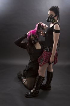 crazy looking teenage girls wearing goth inspired clothes with pink, black hair and gas mask, as the master pulls on the hair of the slave