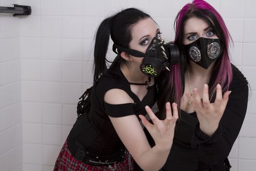 crazy looking teenage girls wearing goth inspired clothes with pink and black hair and gas mask  against a white ceramic wall