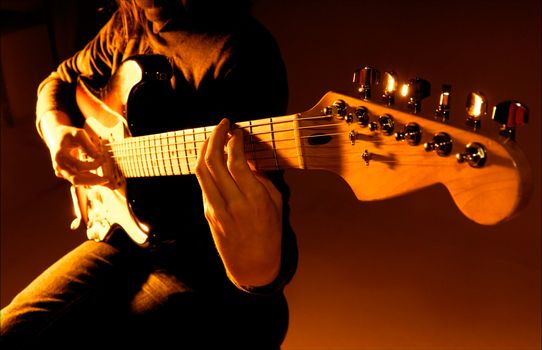 Musician playing guitar at studio with shallow depth of field and orange lighting. 