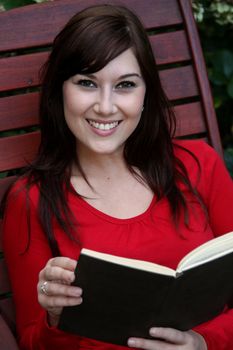 Gorgeous brunette woman on wooden slatted chair reading a book