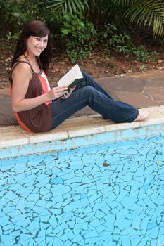 Pretty lady reading a book next to the swimming pool