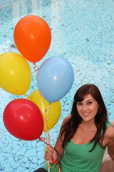 Beautiful woman holding a bunch of balloons next to a swimming pool