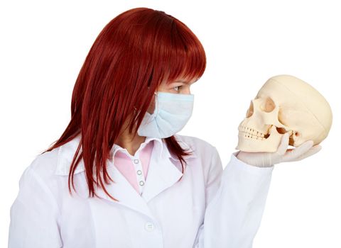 A woman in medical uniform looks at human skull on white