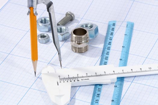 Divider, pencil, caliper, ruler and few screw nuts on graph paper background