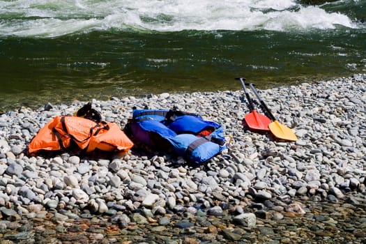 two  life-jackets and two paddles near river
