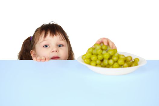 A child reaches for the grapes lying on the table