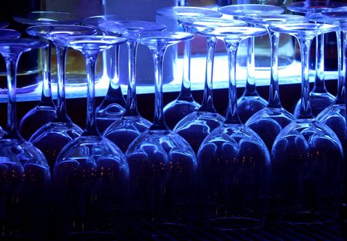 Wine glasses backlit with blue light and bottles in the background