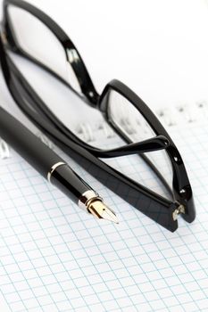 Closeup of fountain pen and  black spectacles lying on open spiral notebook