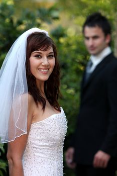 Beautiful smiling bride with her husband our of focus in the background