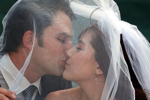 Happy wedding couple kissing under the bride's veil
