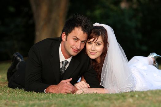 Beautiful wedding couple laying down outdoors on the grass