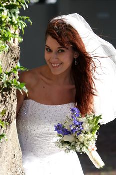 Stunning bride with gorgeous smile standing next to a tree